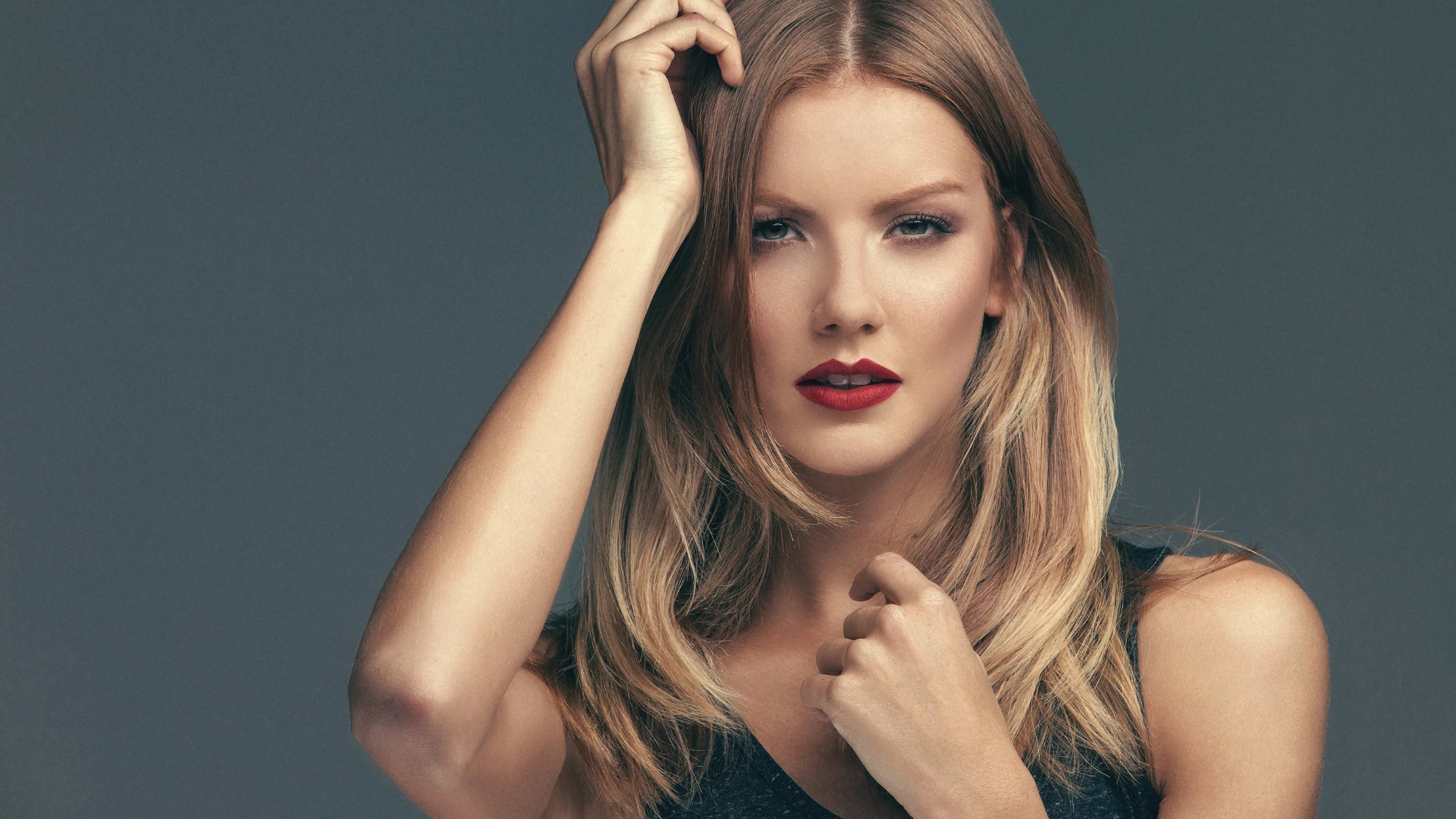 Confident woman with radiant skin and red lipstick posing against gray background